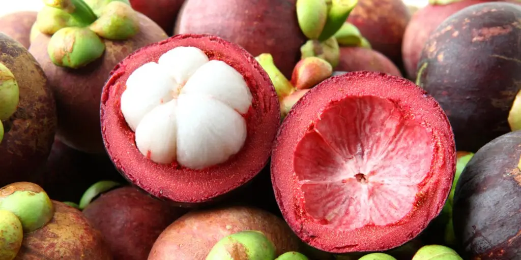 Čerstvý mangostan v košíku, s jedným plodom rozrezaným na polovicu, odhaľujúcim bielu dužinu